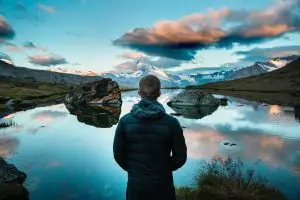 man looking out over lake with reflective surface